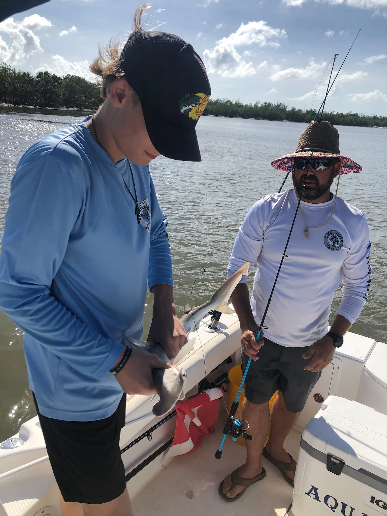 Two people on a boat preparing fishing gear on a sunny day.