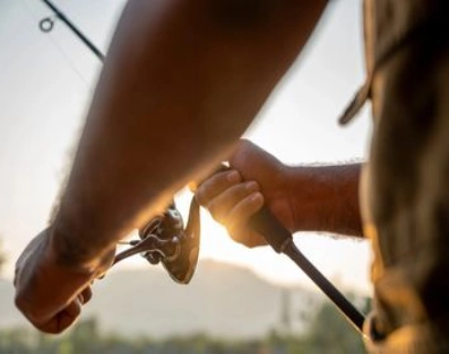 Close-up of hands gripping a fishing rod during sunset.