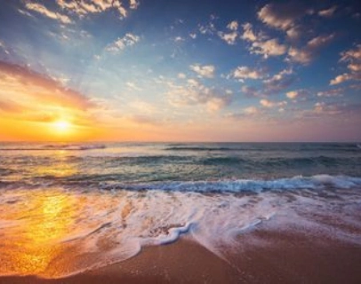 Sunset over a calm ocean with gentle waves on the beach.